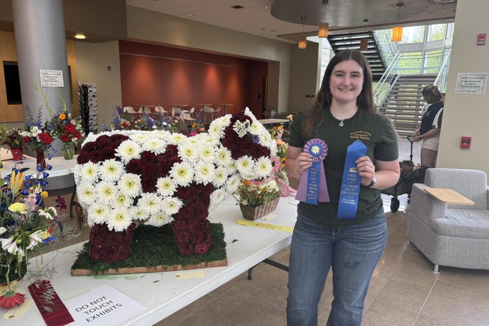 A student is holding a first place ribbon at the fair for her floral arrangement. 