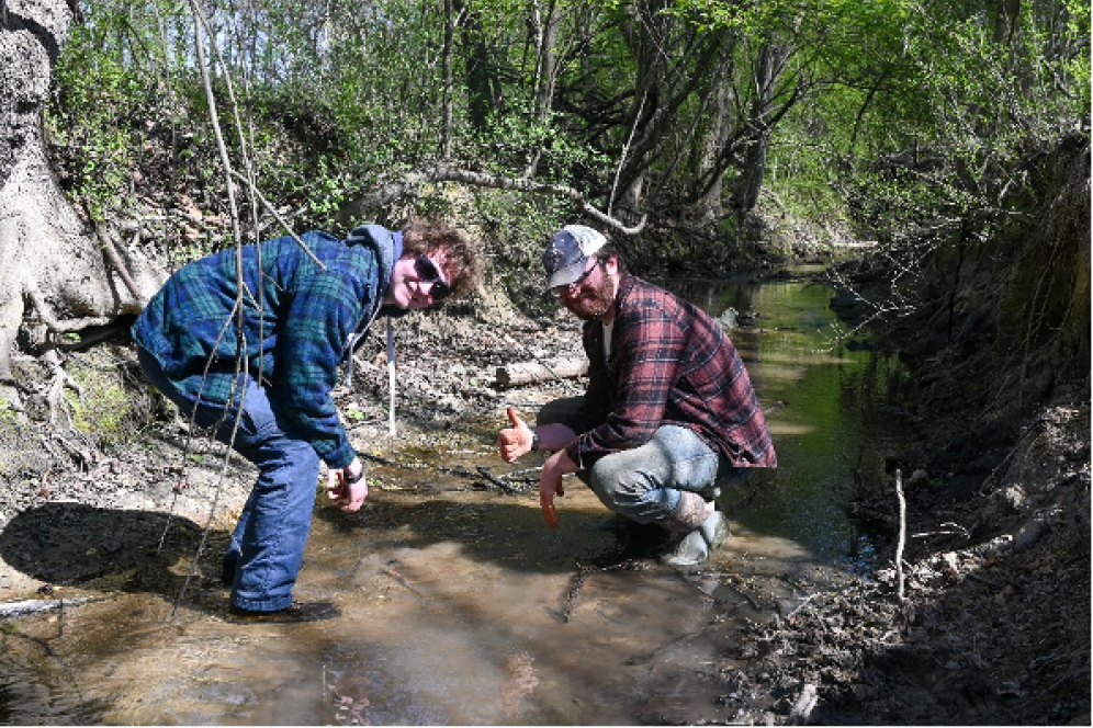 Two Soil Judging Students are taking water samples by a creek of flowing water. 