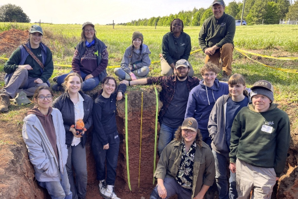 The entire soil judging team of 13 students are in a soil pit smiling at the camera.