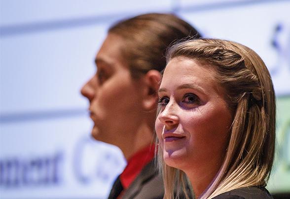 Two students standing on a stage with a financial information behind them on a screen during a presentation.