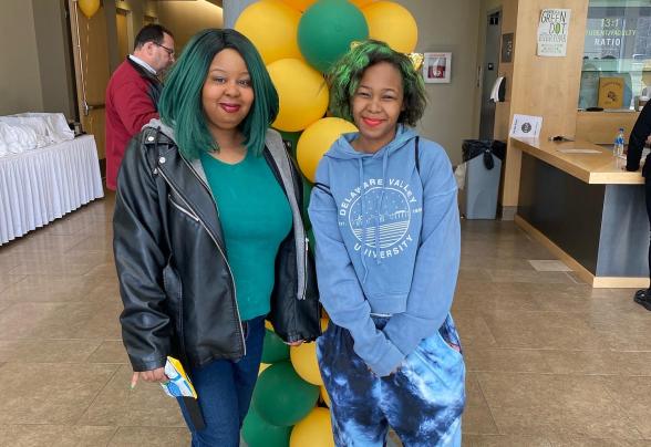 A student and family member at green and gold day in front of ballons 