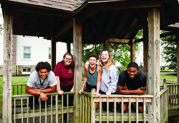 5 students are laughing together in a gazebo on campus.