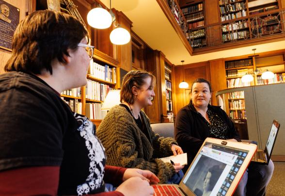 Two students and professor Jessica McCall are in the library talking infront of a computer.