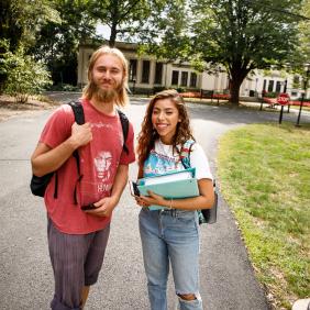 2 students walking on campus, one holding books