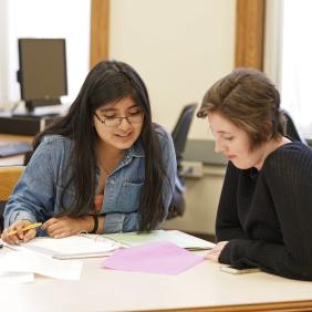 Two female students sitting at a table with notebooks.