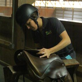 Student adjusting a saddle in the barn