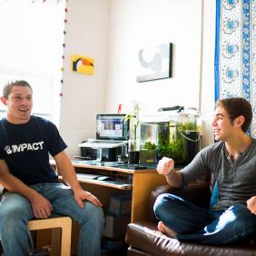 Two male students in dorm room talking and laughing.