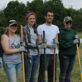 A small group of student holding garden tools.