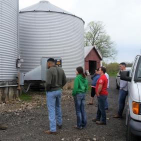 Students learning in the field standing at silos.