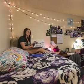 dorm homepage image - young lady sitting on her dorm bed