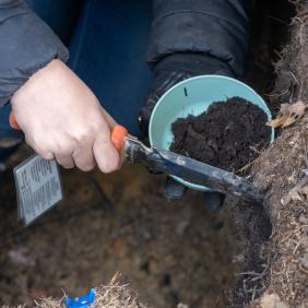 A closeup photo of a student scraping soil for a sample. 