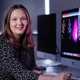 A female student is showing her graphic design project on a mac computer in the media lab. 