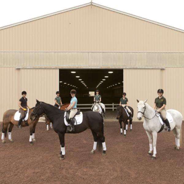 A group of students sit on dressage horses outside of a barn
