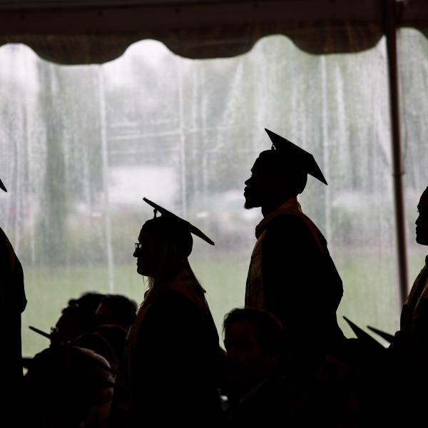 Silhouetted graduates process in a tent