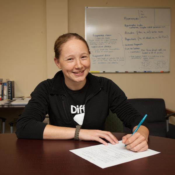 Abree Merch smiling whitle writing a paper with pen and paper.