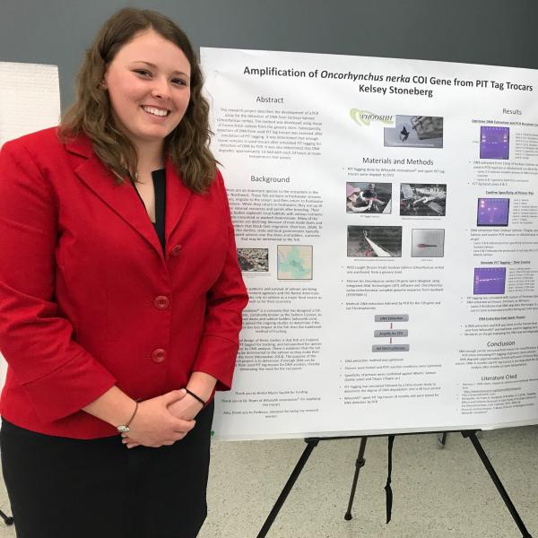 A student wearing a red jacket standing next to a presentation board.