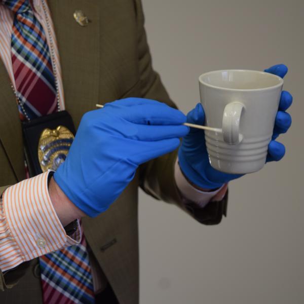 Gloved hands swabbing a coffee mug