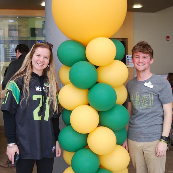 A mother and son pose smile together in front of green and gold balloons.