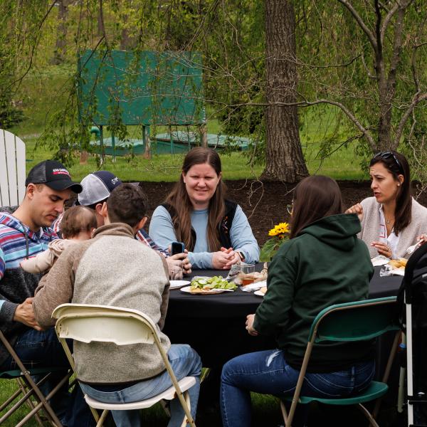 Alumni are seated at a round table eating lunch in front of Lake Archer.