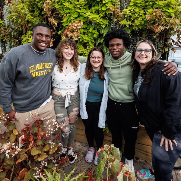 A diverse group of students are in the greenhouse posed for a group photo. 
