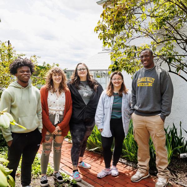 five diverse Terrain intern students posing for a photo by the greenhouse