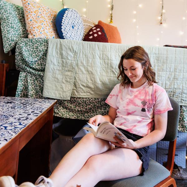 A student is reading a book on a lounge chair. 