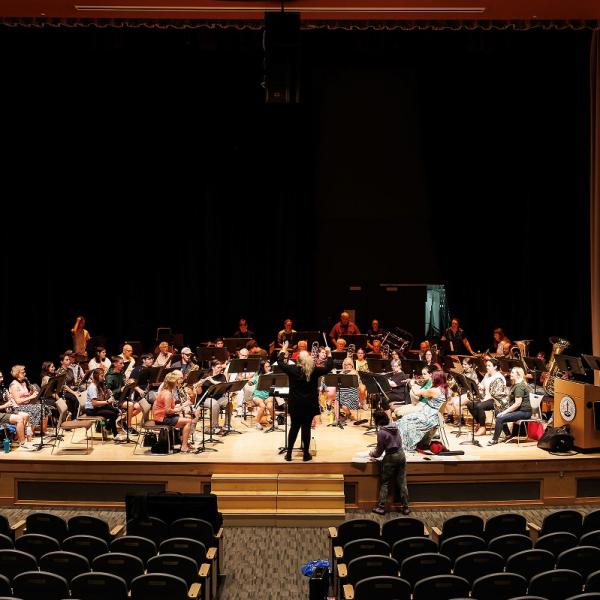 A wide image of the entire symphonic band playing on stage, and watching the direction of the music director. 