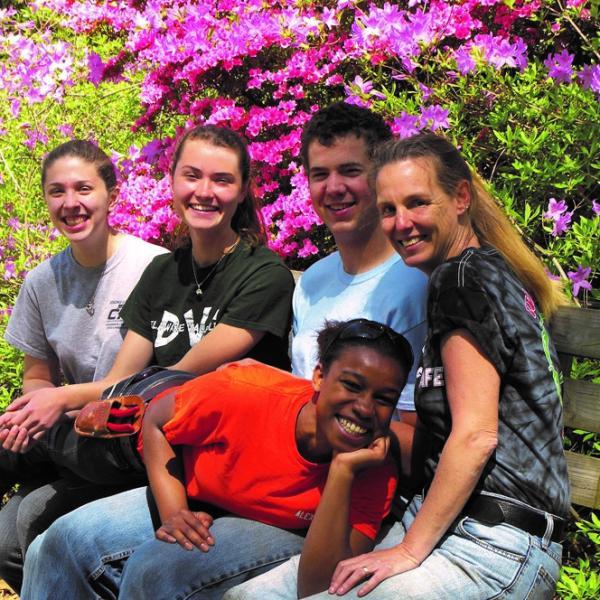 Five students are smiling at the camera while sitting on a bench. 
