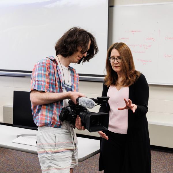 Media and Communication professor Marion Callahan is teaching a student how to use a video camera.