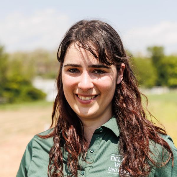 A headshot of jaclyn fiola wearing a delval green collared shirt in a field of soil. 