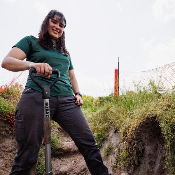 Dr. Jaclyn Fiola in a soil pit with a shovel, smiling at the camera. 