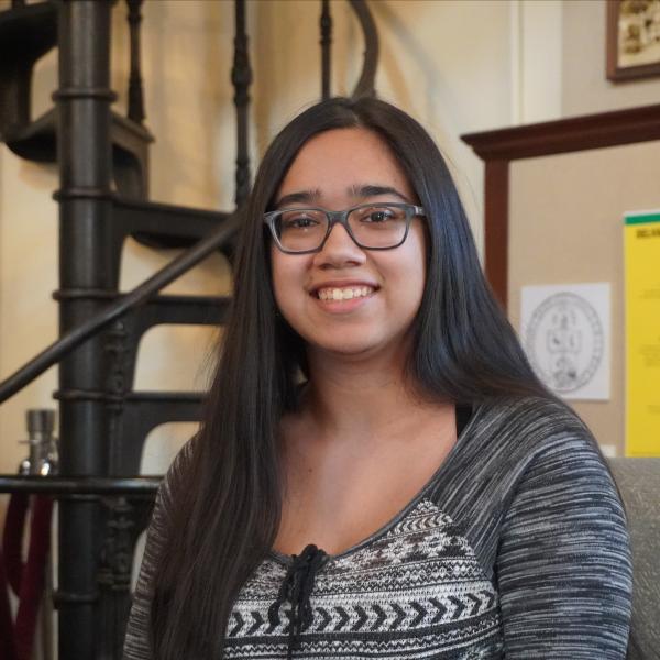 Athena Castro sitting in the library memorial room smiling at the camera. 