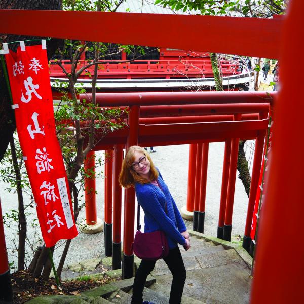 A student is in japan by a banner with japanese writing. 