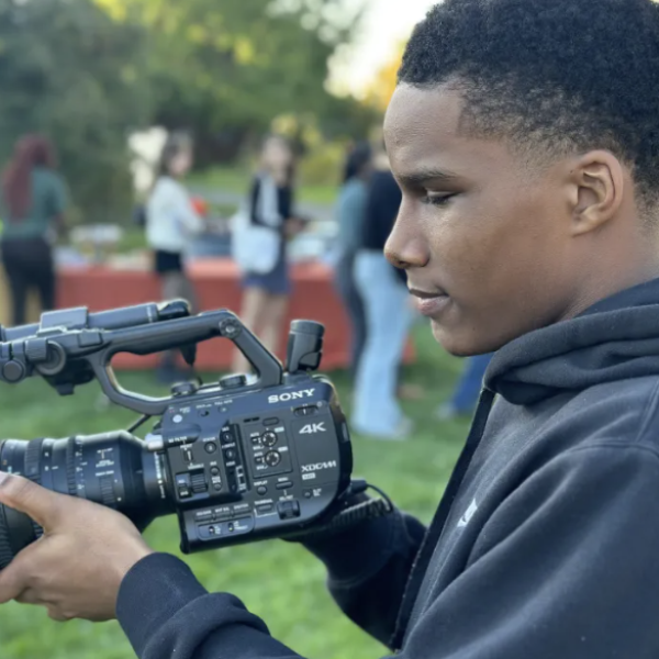 A student from the student media club is holding a large video camera.