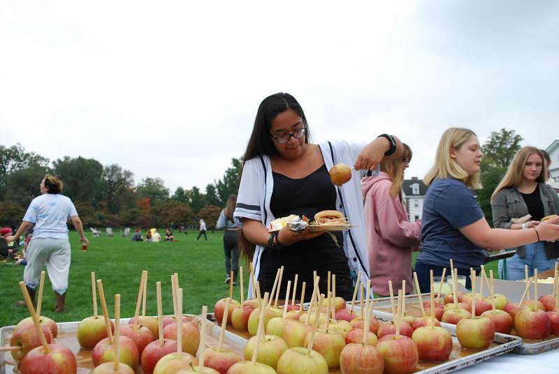 A student is taking an apple glazed in caramel from a table full of caramel apples. 