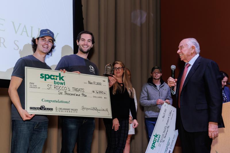 Kaleb and Kolby Rush, founders of Saint Roccos Treats hold a giant check on stage. 