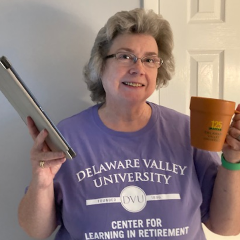 CLR Member holds a mug and her laptop. She is wearing a DelVal CLR purple shirt.