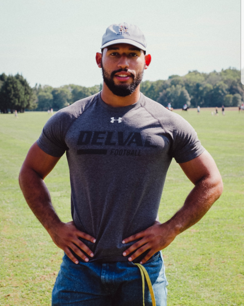 Nigel Feliz wearing a delval tshirt and cap standing on the quad.