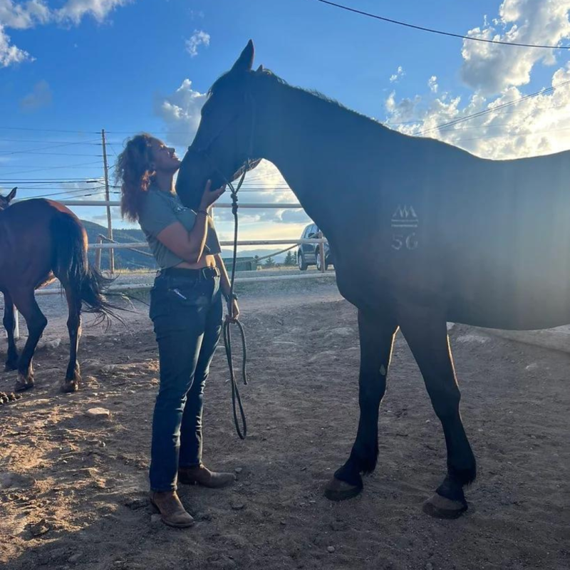 Jasmine Coates '22 an african american woman wearing a hat standing with two horses.