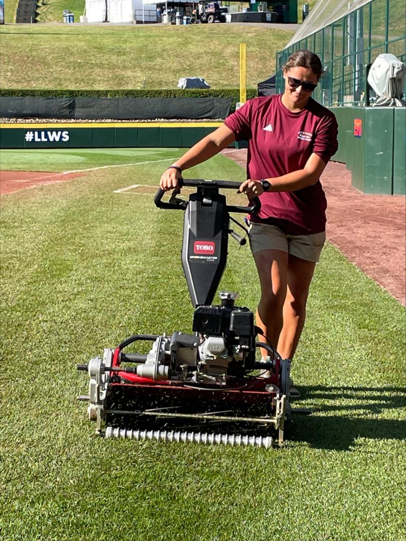 Jillian is working a machine at the little league world series on the turf. 