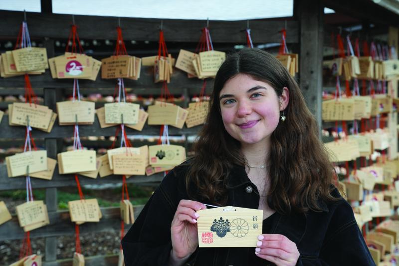A female student is in Japan holding a card with Japanese art written on it. 