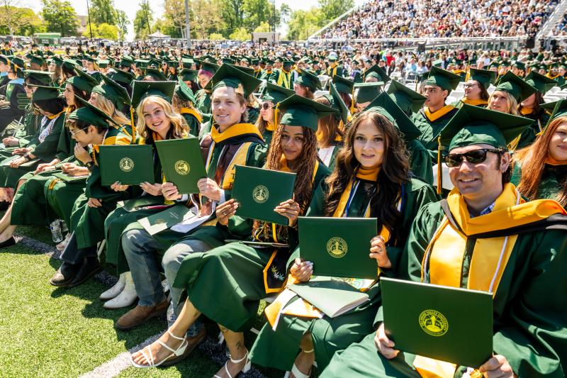 Graduates sitting holding their diploma holders in their green caps and gowns at DelVal's 2026 Commencement.