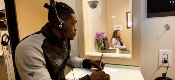 A student taking notes on the other side of the glass during a mock counseling session
