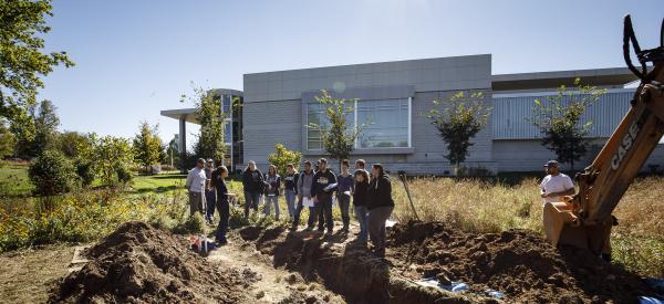 A group of students at Delaware Valley University examining soil outside on campus in front of the Life Sciences Building.