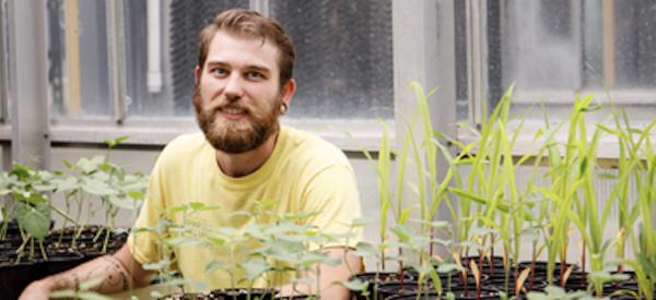 Student in a greenhouse in between two tables of plants