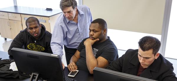3 college-aged students and a professor having a discussion and looking at a computer 