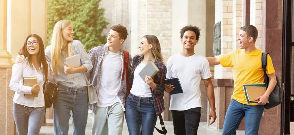 A group of 8 students walking in front of building carrying their books and smiling.