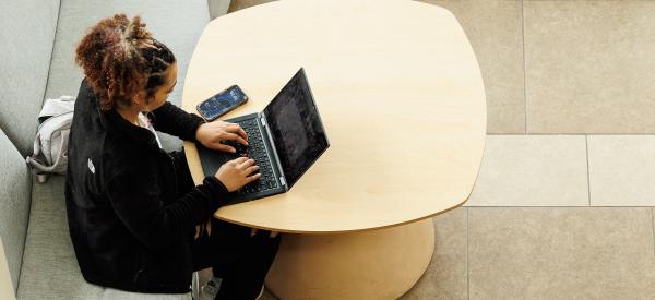 A student is working on a laptop and notepad with pencil in hand.