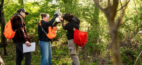 Three students are outdoors with notepads and equipment during a conservation course.