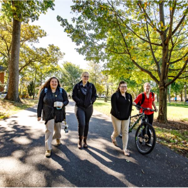 four college-aged students walking together under some trees